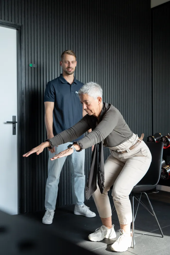 Oudere vrouw doet een squat-oefening onder begeleiding van een fysiotherapeut